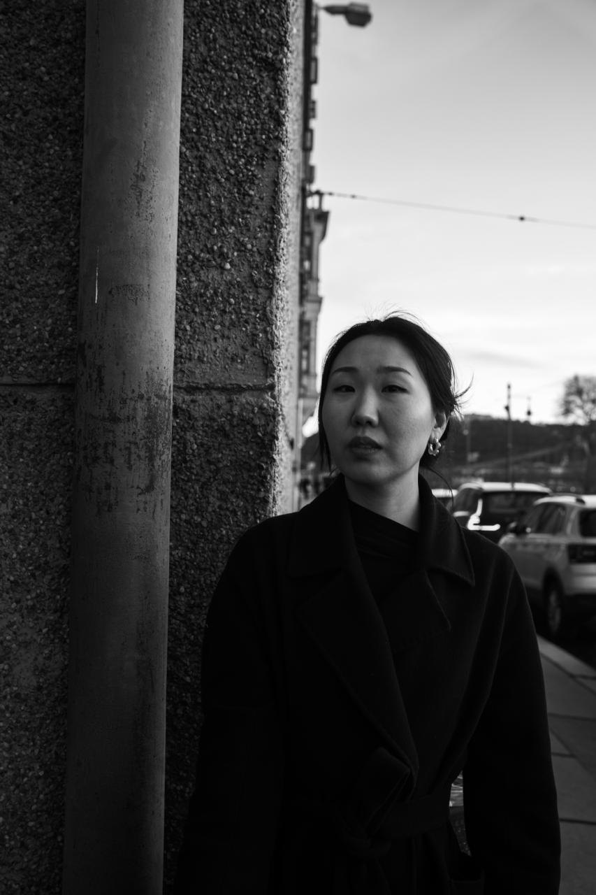 A woman in a long coat on a street, in black and white