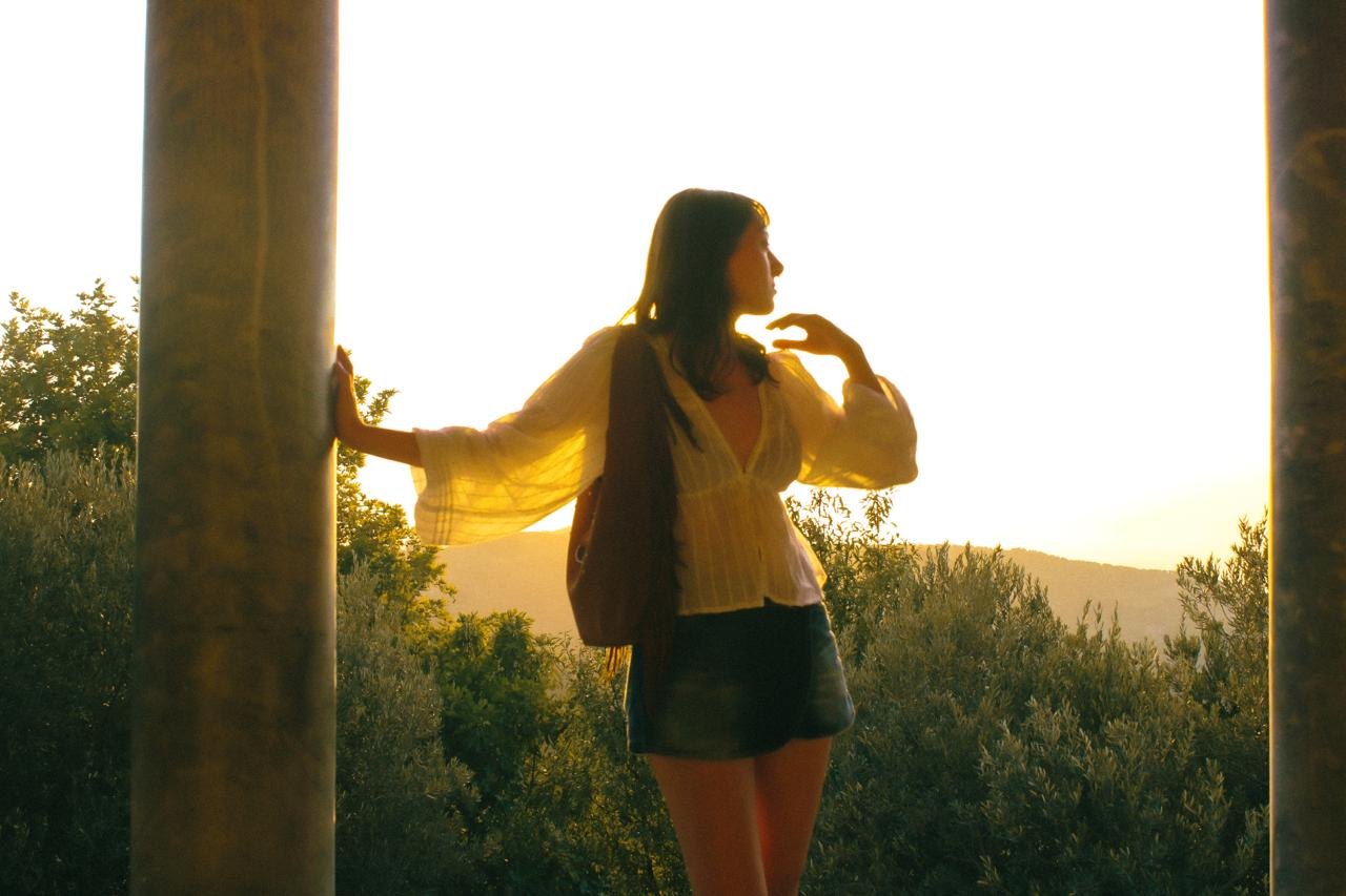 A woman in a yellow cardigan in low sunlight, one hand on a pillar