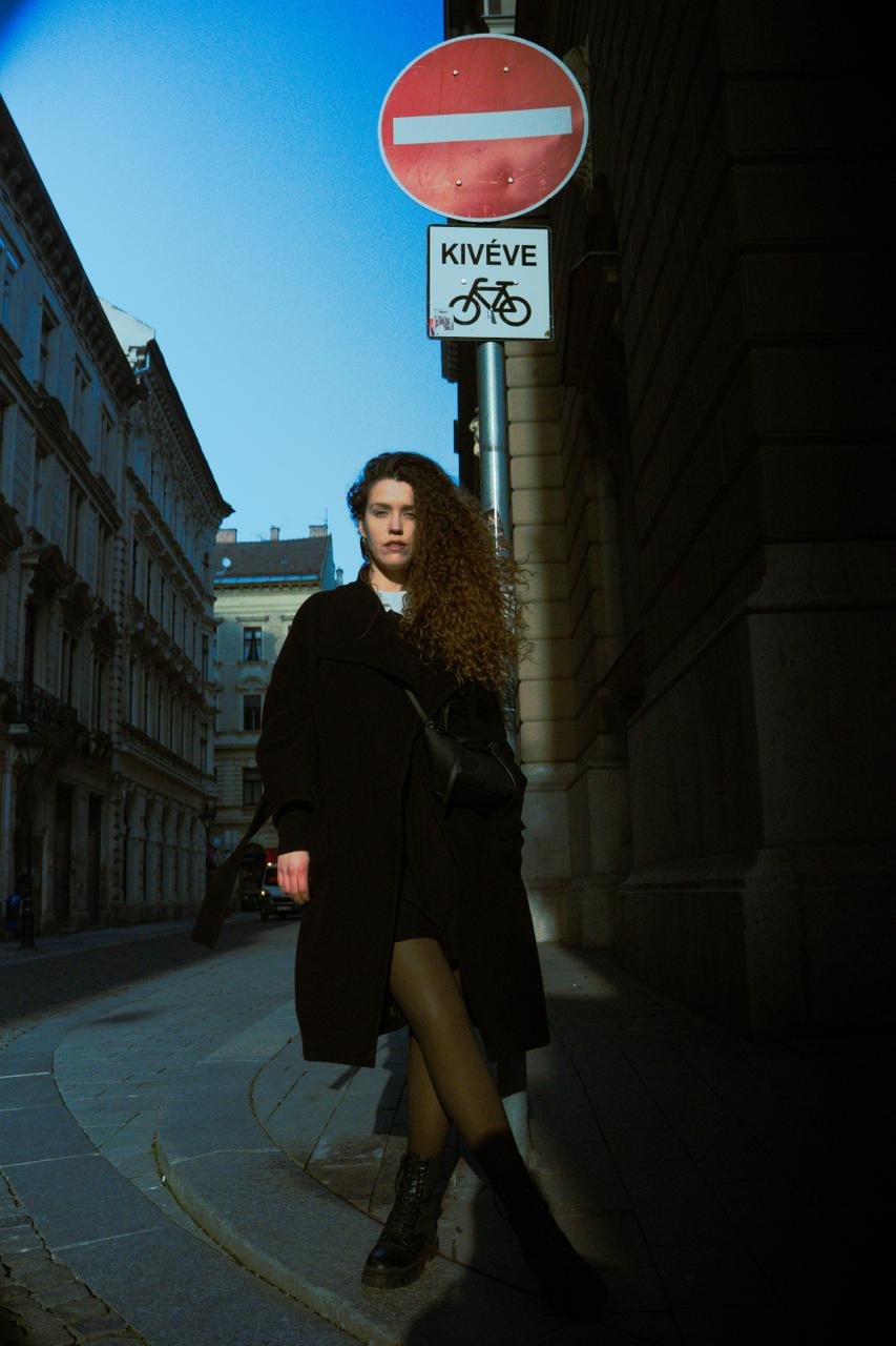 A woman in a long coat on a street below a no-entry sign