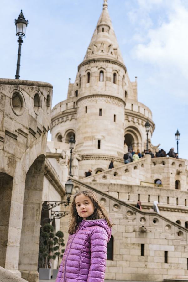 A girl in a purple jacket in front of a tower of Fisherman's Bastion