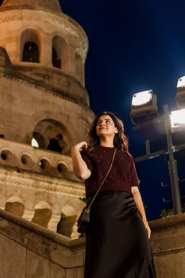 A woman looking up at night below a lit tower of Fisherman's Bastion