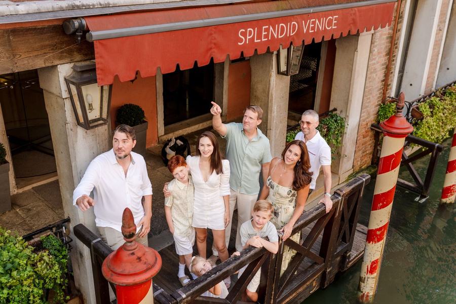 A family on a canal-side landing below a red awning, seen from above, a man pointing up
