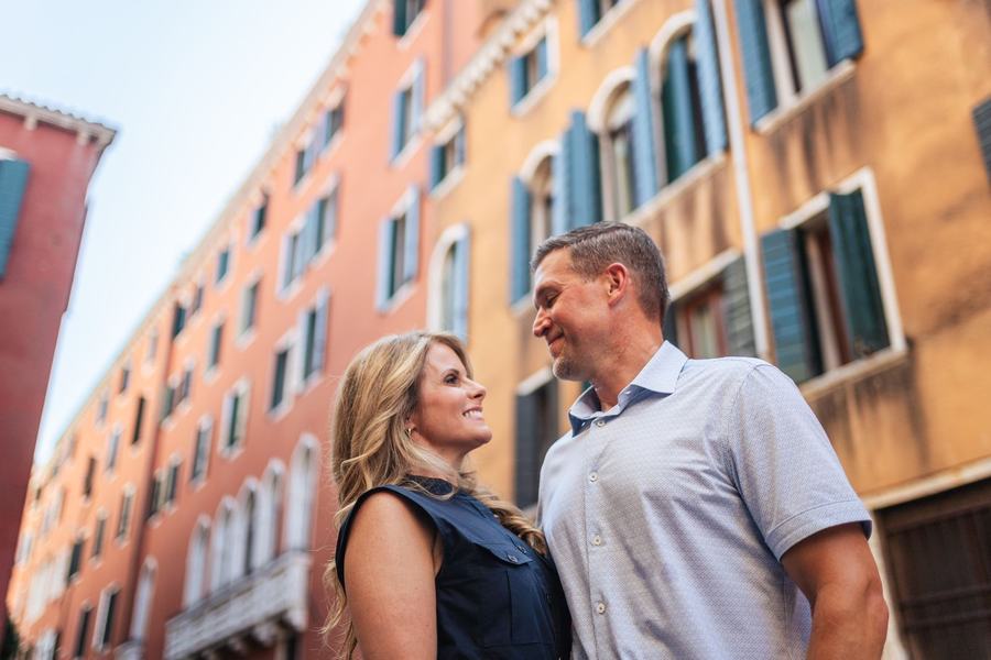 A couple smiling at each other below tall orange and red Venetian houses