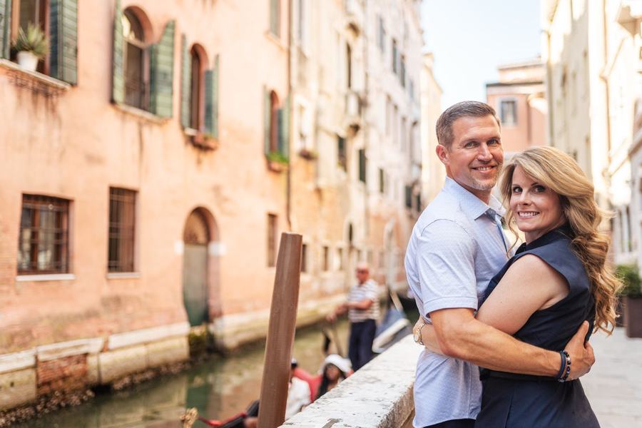 A couple hugging beside a canal in Venice, smiling at the camera