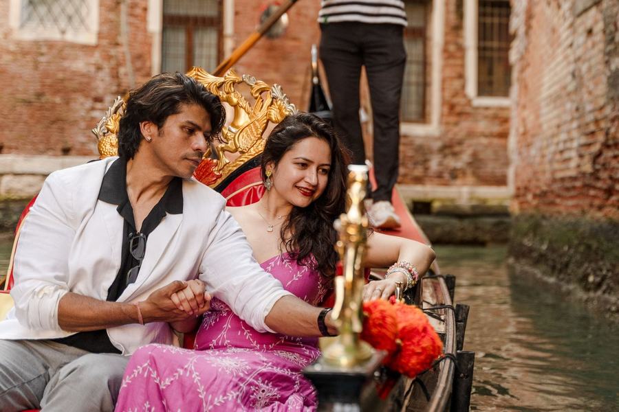 A couple holding hands on a gondola in a narrow canal