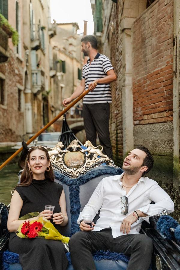 A couple on a gondola looking up at the houses of a narrow canal