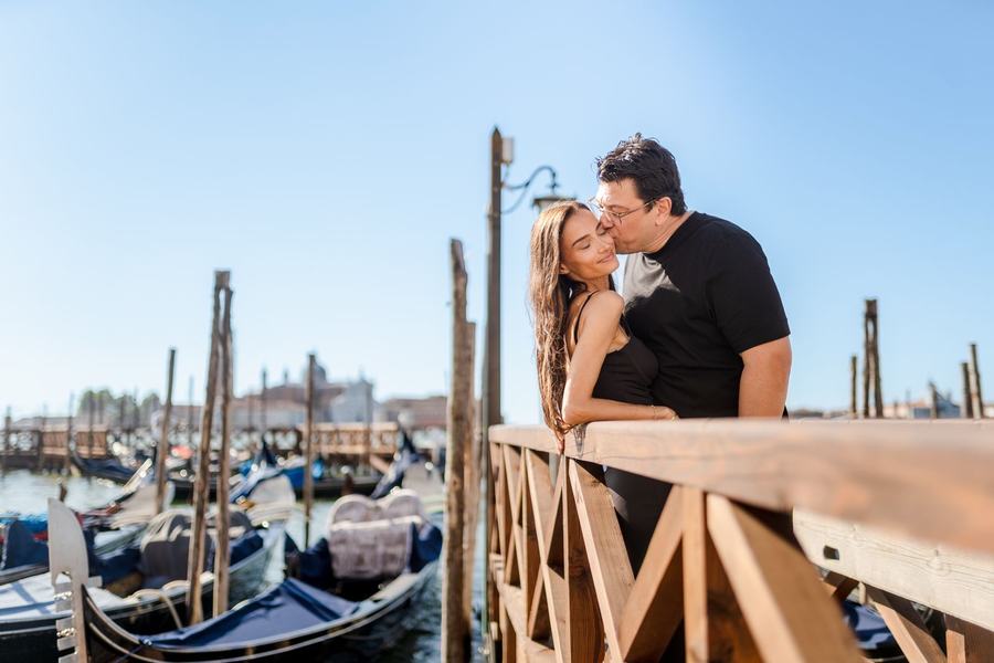 A man kissing a woman's cheek on a pier beside moored gondolas