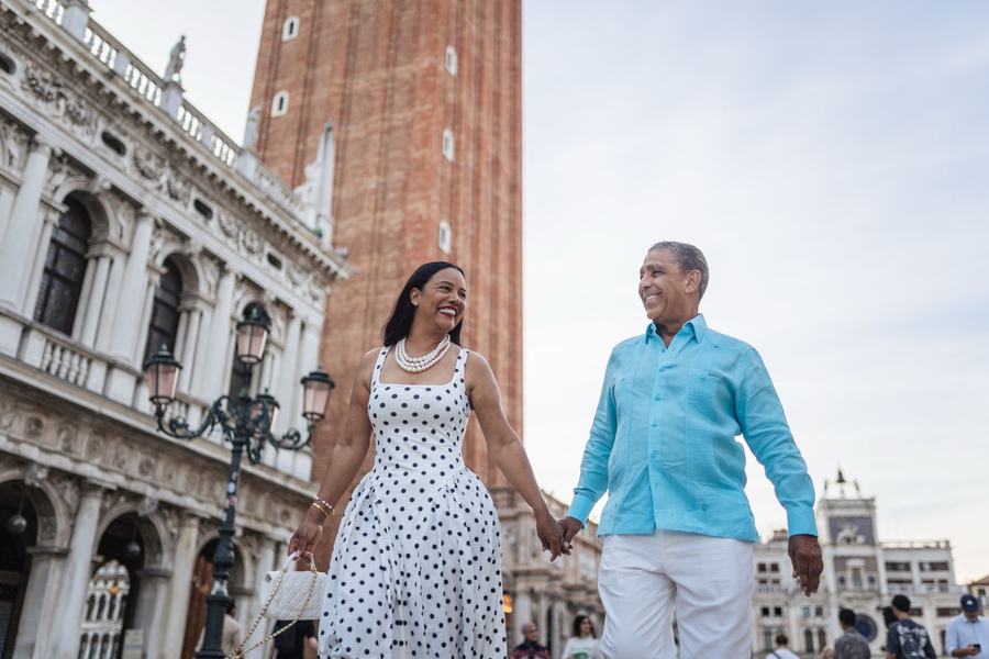 A couple walking hand in hand past the bell tower of St Mark's
