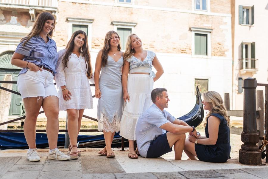 Four sisters standing by a canal while their parents sit and laugh beside a gondola