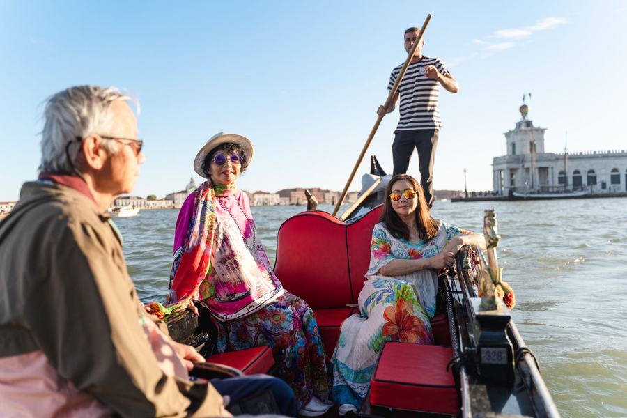 A family on a gondola on the lagoon, the Punta della Dogana behind them