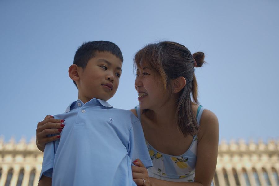A mother and her son in St Mark's Square under a blue sky, the Procuratie behind them