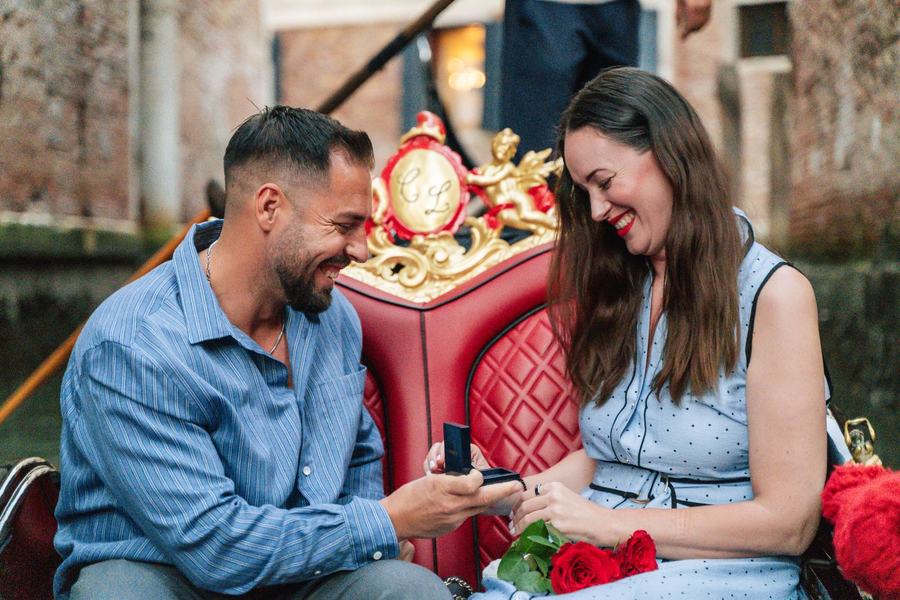 A man opening a ring box for a laughing woman on a gondola