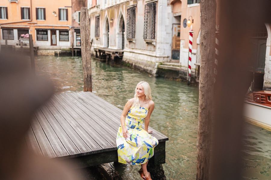 A woman in a yellow dress sitting on a wooden pier over a Venetian canal
