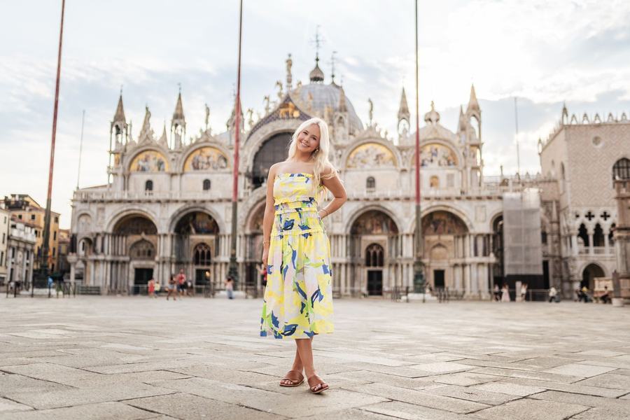 A woman in a yellow dress standing in St Mark's Square in front of the basilica