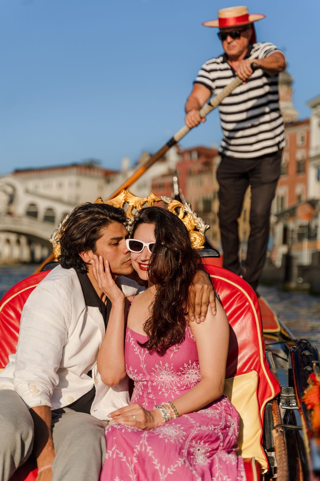 A man kissing a woman's cheek on a gondola, the Rialto Bridge behind them